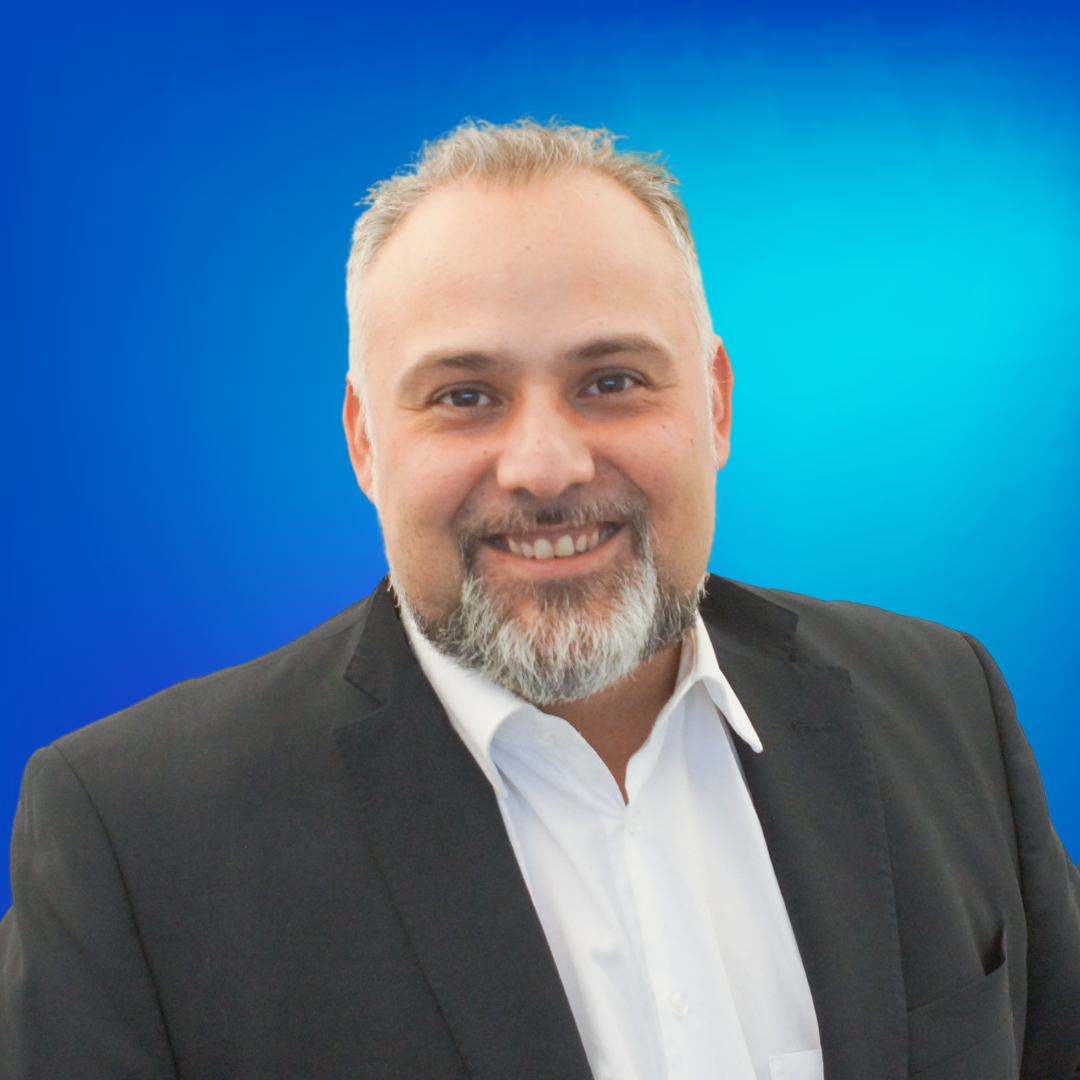 Porträt eines lächelnden Mannes mit Bart und Anzug vor blauem Hintergrund.