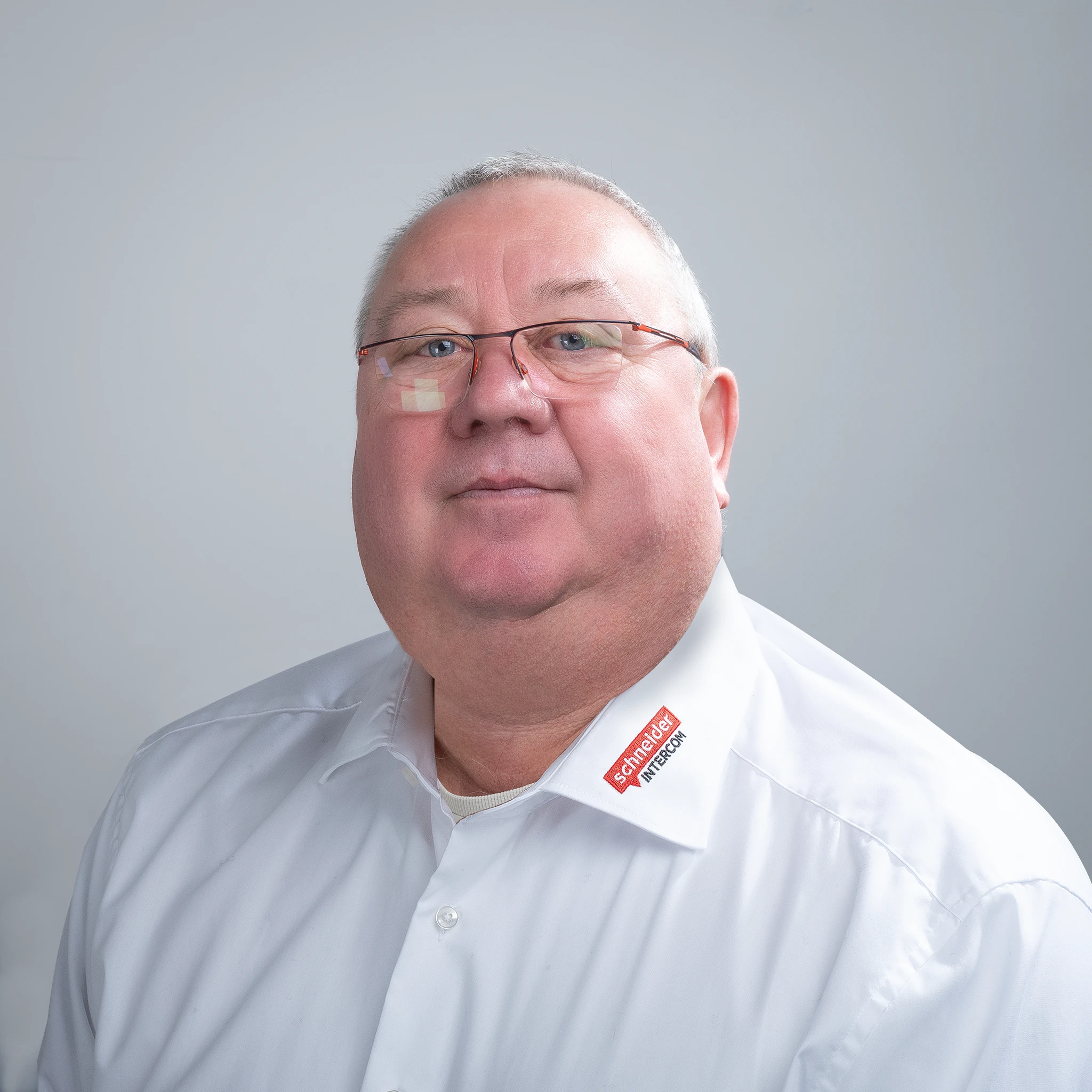 Mann mit grauem Haar, Brille, weißem Hemd, "Schneider Sprechanlagen" Logo.