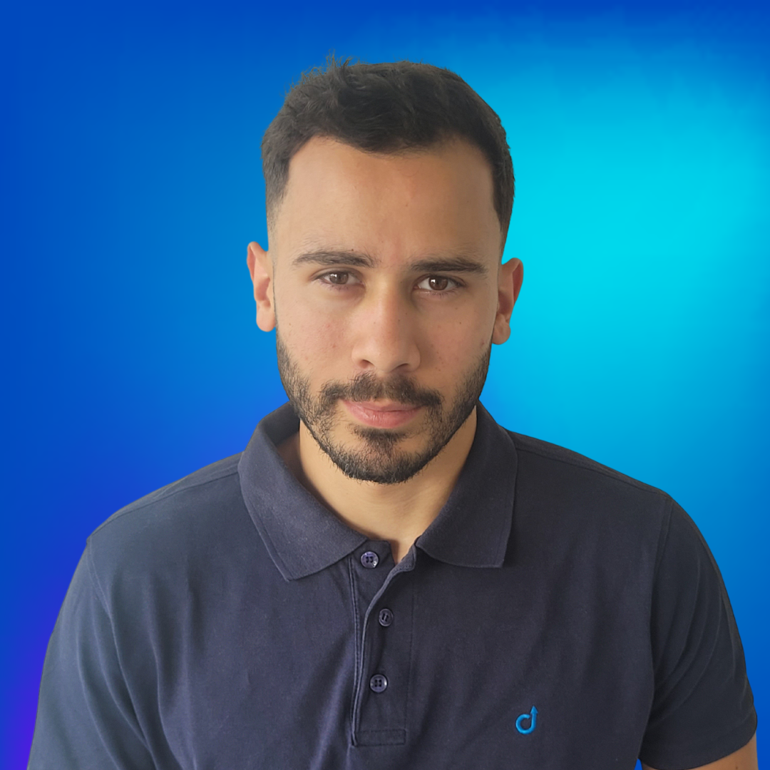 Junger Mann mit Bart in dunkelblauem Poloshirt vor blauem Hintergrund.