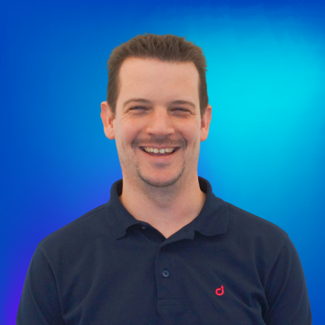 Kopfaufnahme eines lachenden Mannes in dunkelblauem Poloshirt vor blauem Hintergrund.