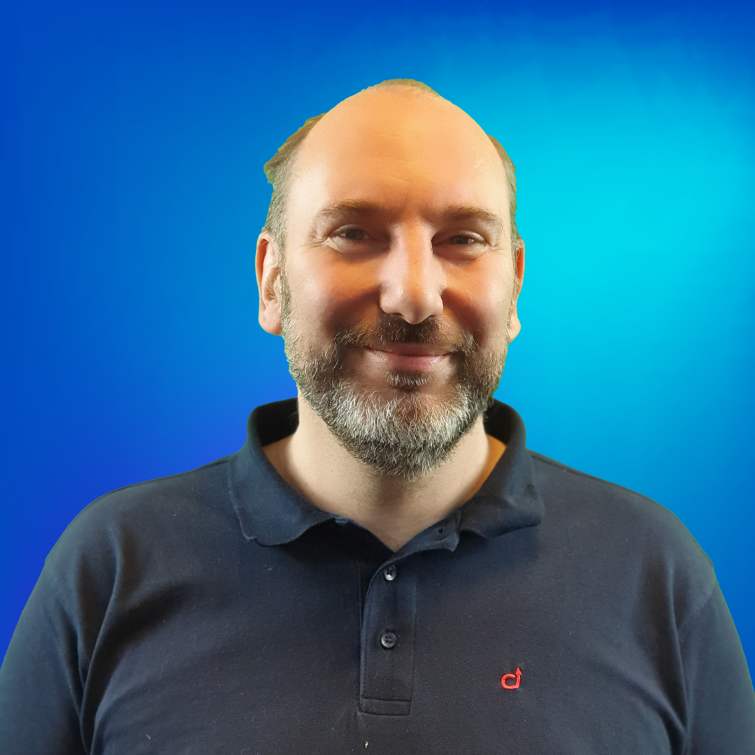 Ein lächelnder Mann mit Bart und dunklem Poloshirt vor blauem Hintergrund.