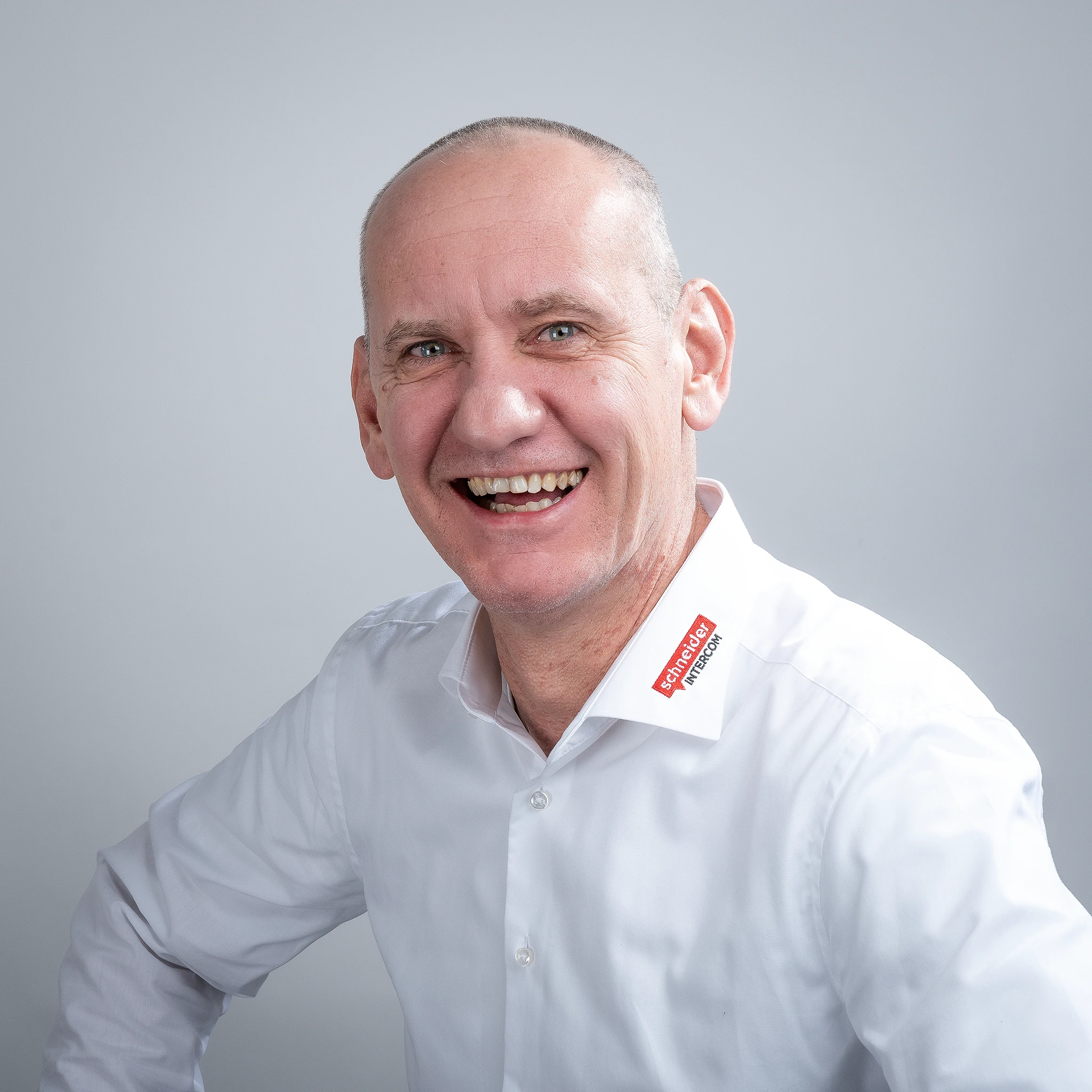 Lächelnder Mann mit Schneider Intercom-Logo auf weißem Hemd. Er steht für zuverlässige Kommunikation.