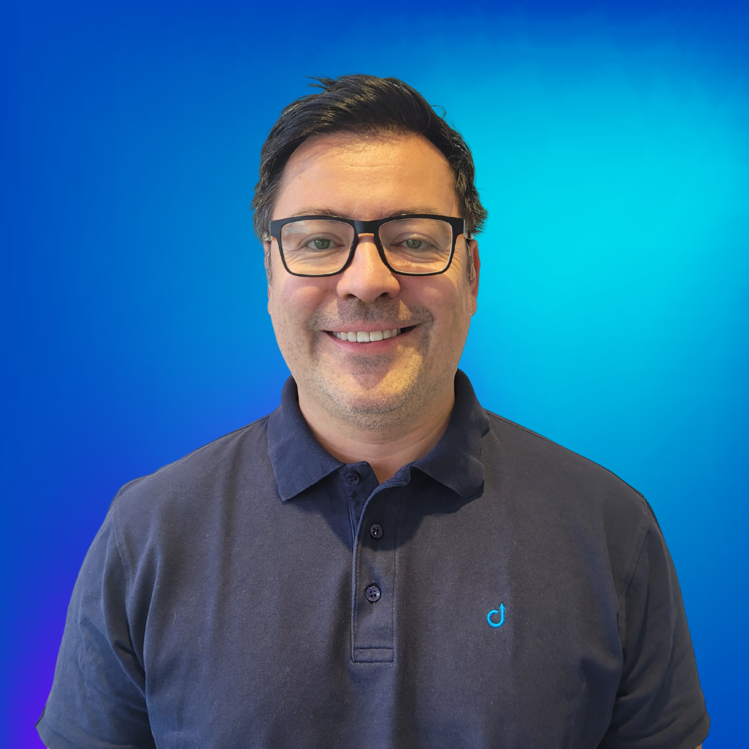 Porträt eines lächelnden Mannes mit Brille in einem dunkelblauen Poloshirt vor blauem Hintergrund.