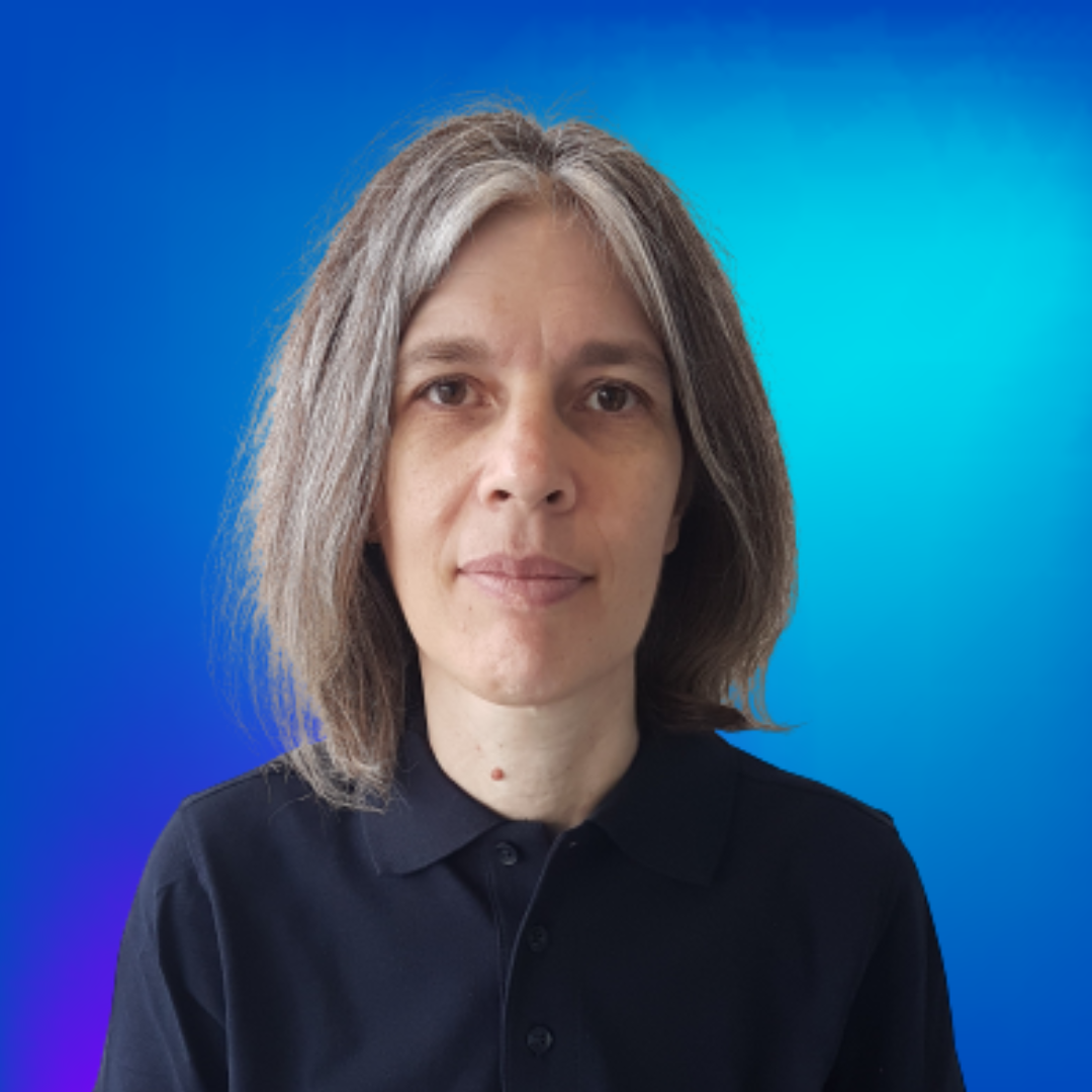 Porträt einer Frau mit grauem Haar und blauem Hemd, blickt ruhig in die Kamera vor blauem Hintergrund.