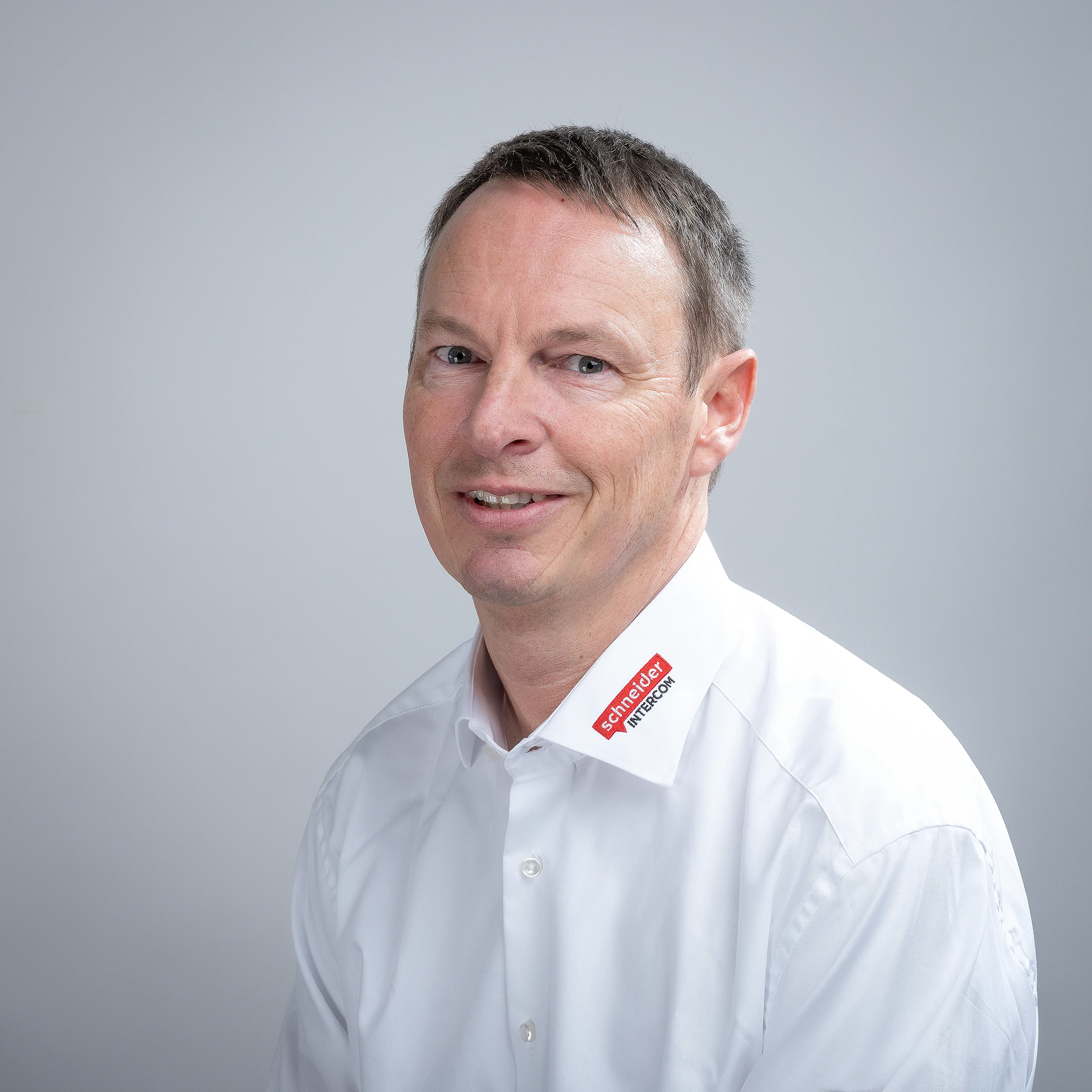 Ein lächelnder Mann im weißen Hemd mit dem Schneider Intercom Logo am Kragen.