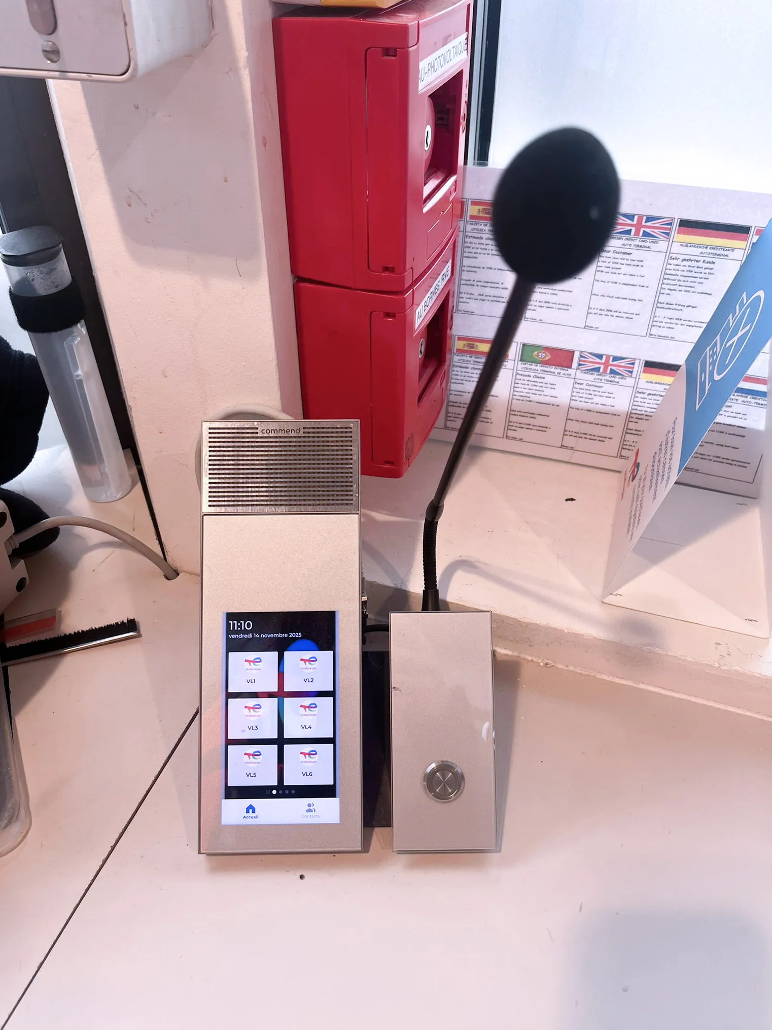 Eine Commend Sprechanlage mit Touchscreen und Mikrofon, daneben rote Notrufsysteme und Informationen.