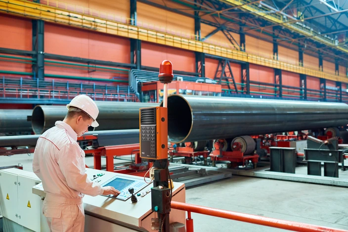 Arbeiter an Industriesteuerung Arbeiter bedient Maschinensteuerung mit integrierter Sprechstelle neben großen Rohren.