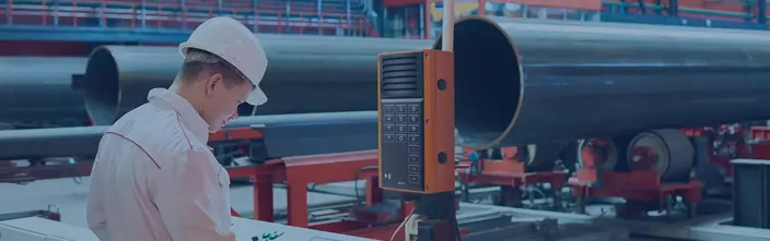 Industrial Intercom for Factory Use Worker at control panel next to an orange industrial intercom in a factory.