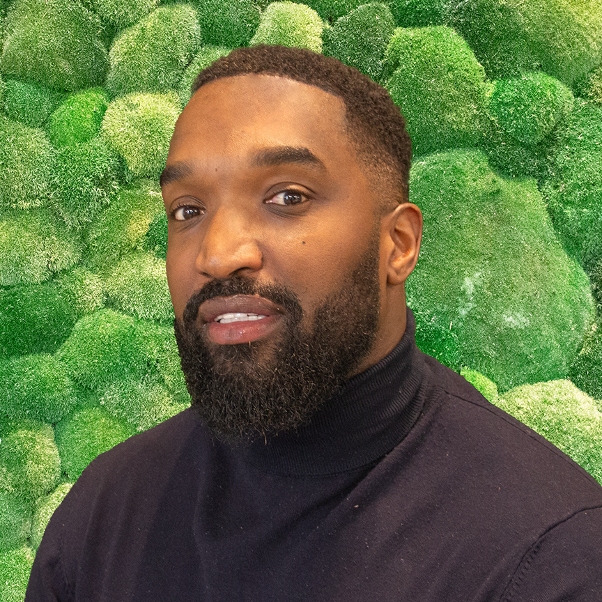 Professional man in black roll-neck against green moss wall.