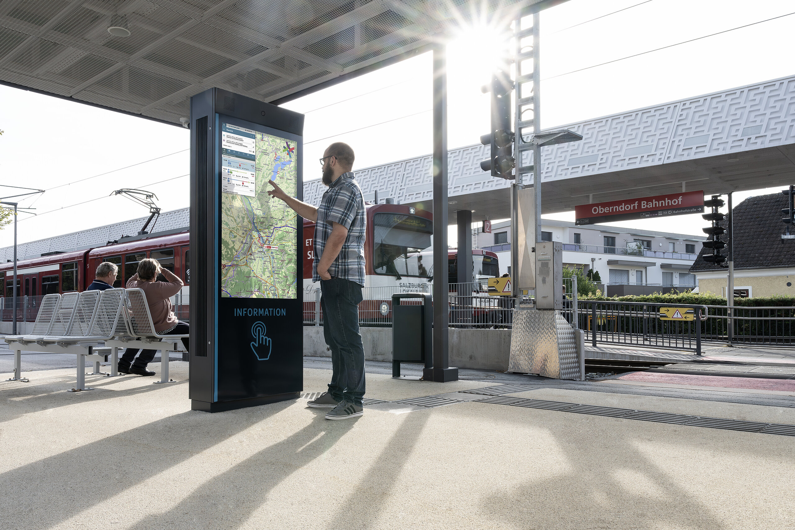 Mann bedient interaktive Infotafel am Bahnhof Oberndorf mit Karte.