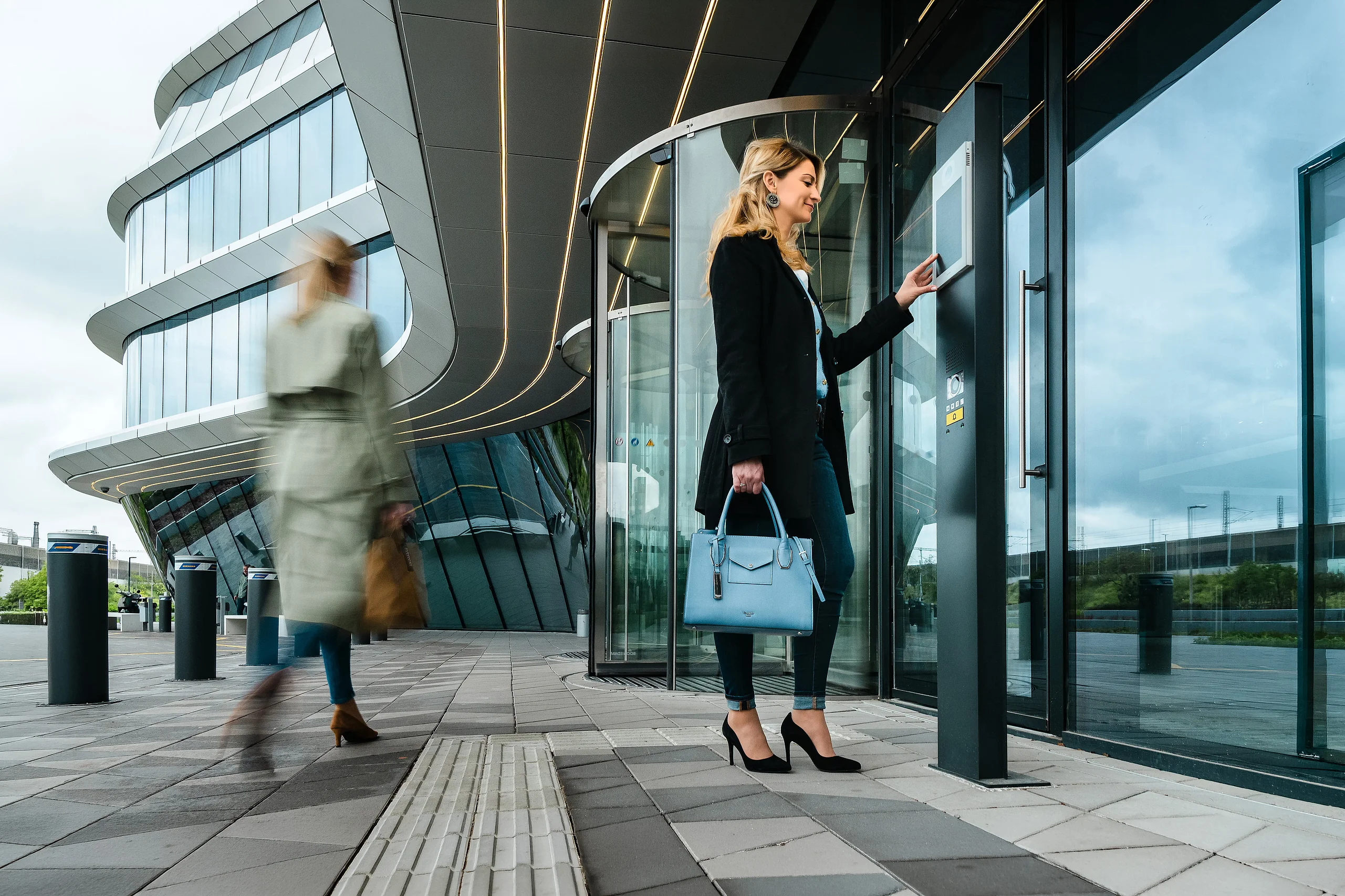 Woman using an Intercom entrance terminal beside the revolving door at MOL Campus in Budapest