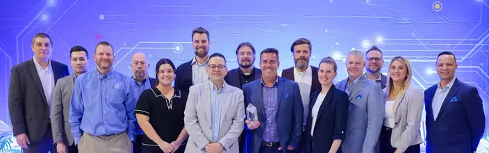Valued Team Wins Award Group of happy businesspeople on stage, one holding a prize, against a blue digital background.