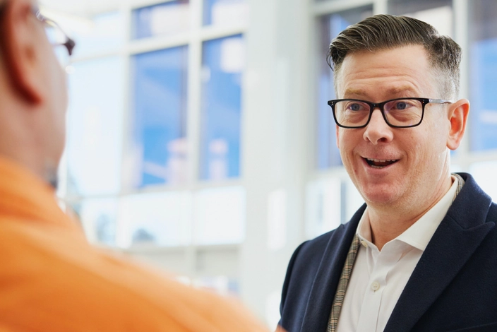 Engaging Business Talk Man with glasses smiling while talking to another person in a modern office.