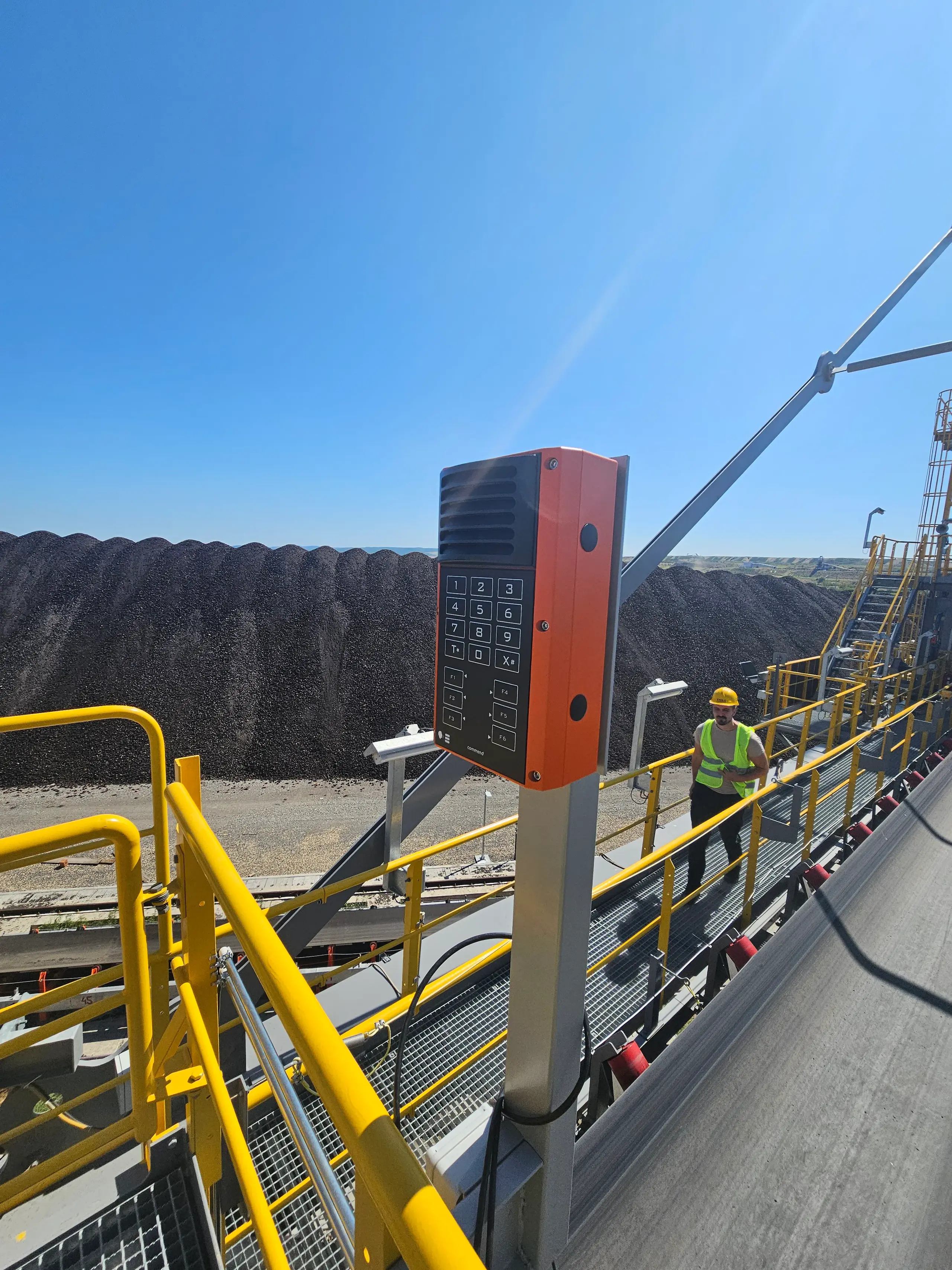 Intercom with keypad mounted on conveyor walkway as worker passes in industrial area Industrial intercom with keypad on conveyor walkway installation