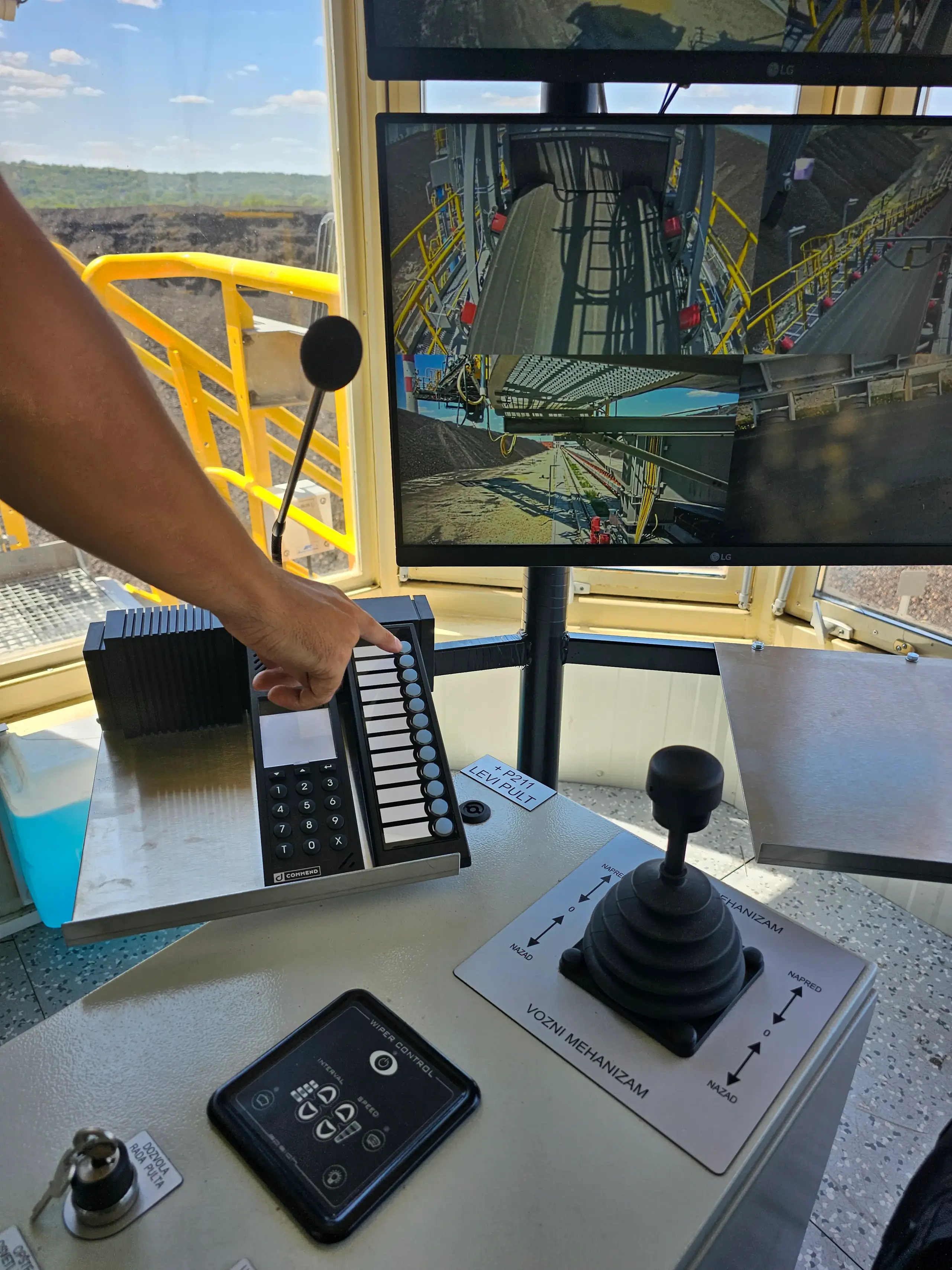 Hand on control panel with intercom, joystick and monitoring screens in control cabin Control panel with intercom and monitoring in industrial control cabin
