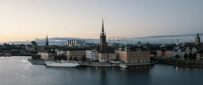 Stockholm Old Town at Dusk Aerial view of Stockholm cityscape at dusk with Riddarholmen Church, old buildings, and a ship on the water.