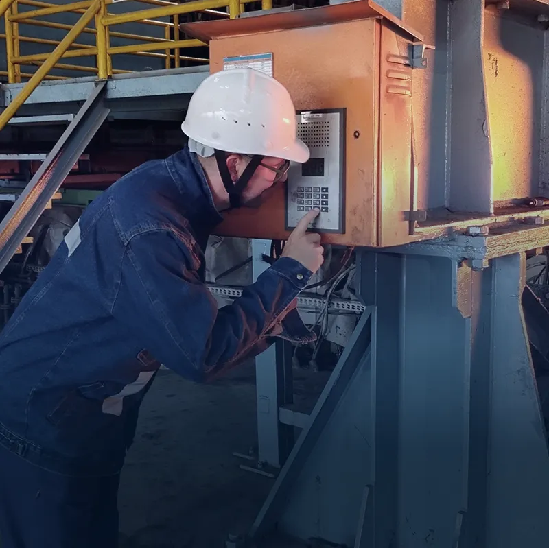 Worker in protective gear operating an industrial intercom mounted on machinery in the plant