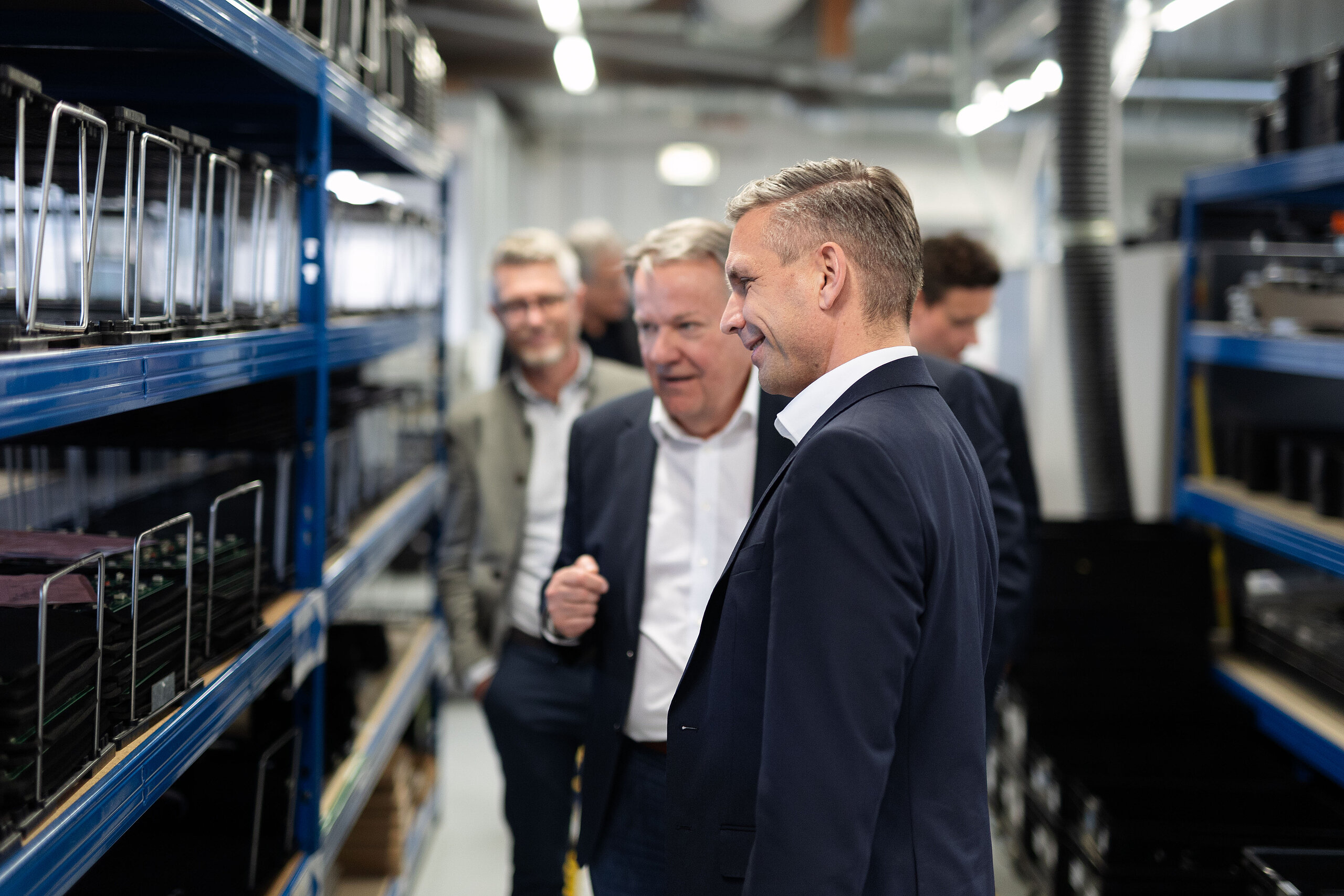 Männer inspizieren Sprechstellen auf blauen Regalen in einer Produktionsanlage.