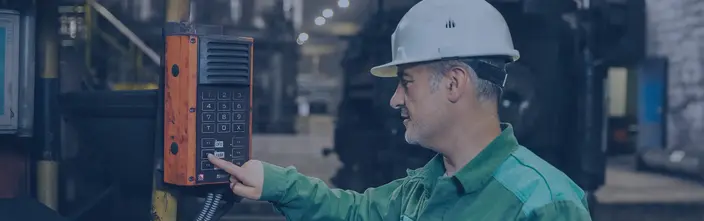 Arbeiter bedient industrielle Sprechanlage Mann mit Schutzhelm bedient orangefarbene Industriesprechanlage in einer Fabrik.