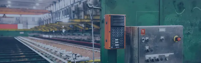Industrial Intercom on Factory Floor Orange industrial intercom and control panel in a factory, with machinery in the background.