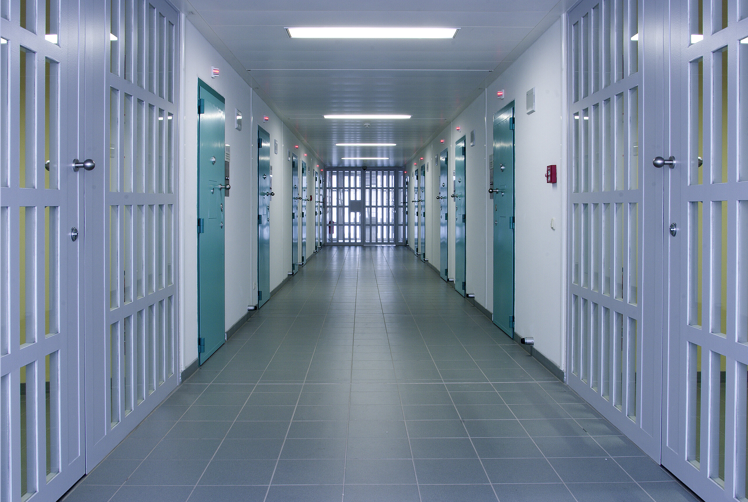 Secure Facility Corridor Long, sterile corridor in a secure facility with many teal doors and a barred gate at the end.