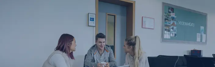 Plauderei neben einer Sprechstelle Drei junge Leute unterhalten sich in einem Gemeinschaftsbereich mit einer sichtbaren Sprechanlage.