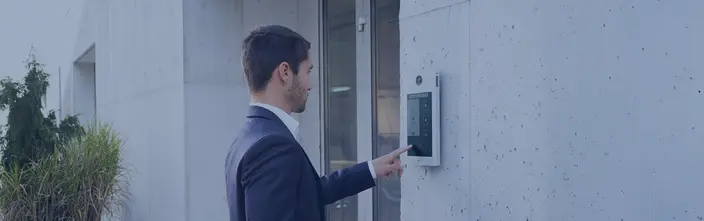 Man interacting with a digital intercom panel outside an office building.